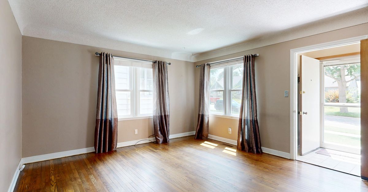Spacious and well-lit empty living room with hardwood floors and open door.