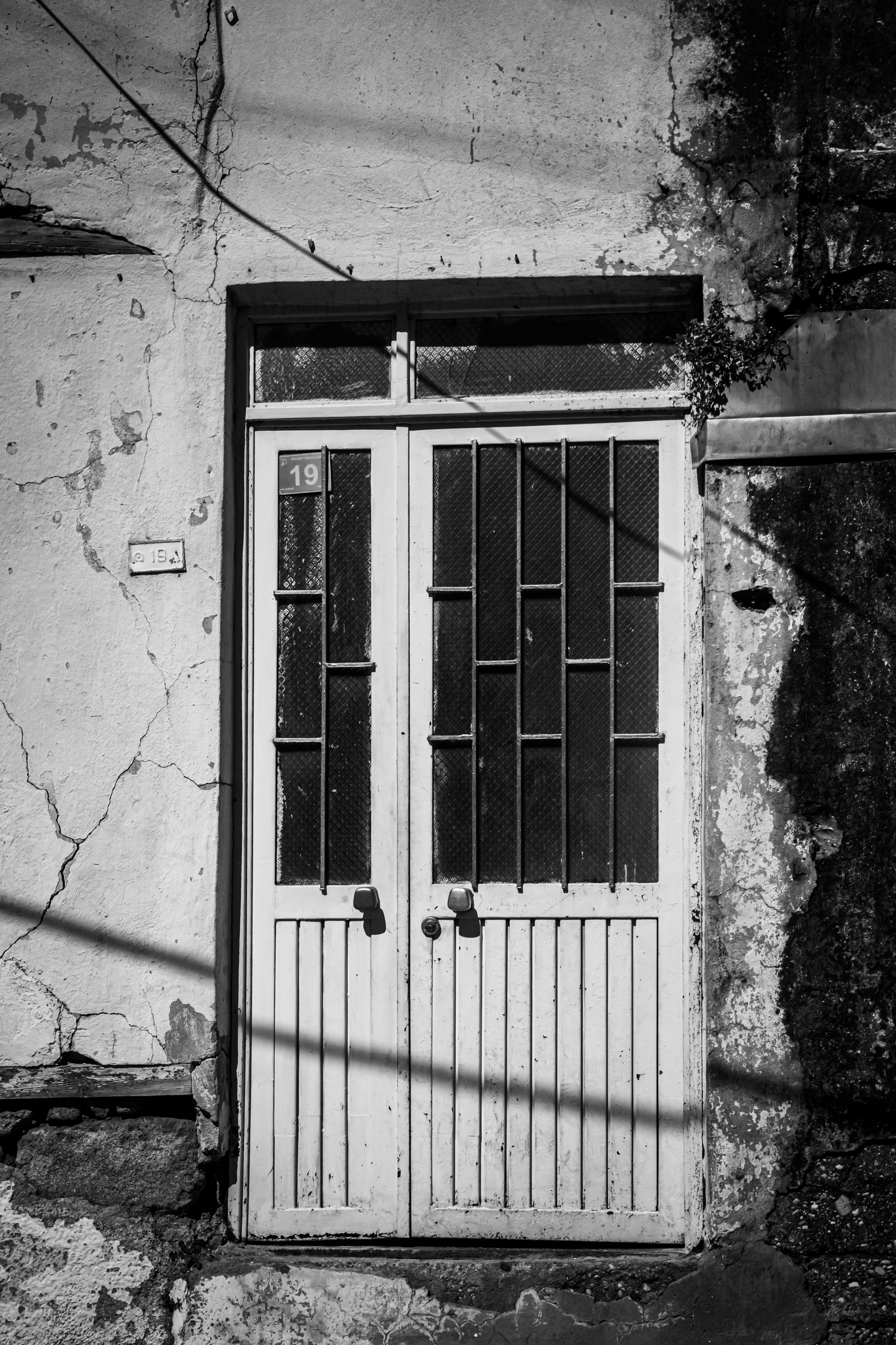 Black and white image of a rustic door on an old, weathered building facade.