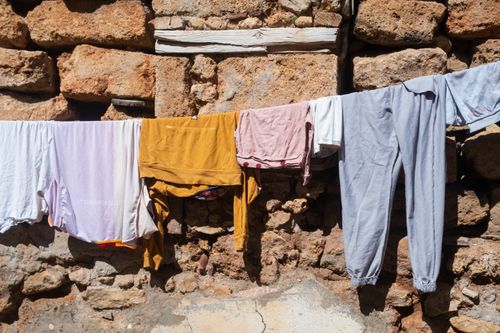 Free Colorful clothes hanging on a line against a rustic stone wall in sunlight. Stock Photo
