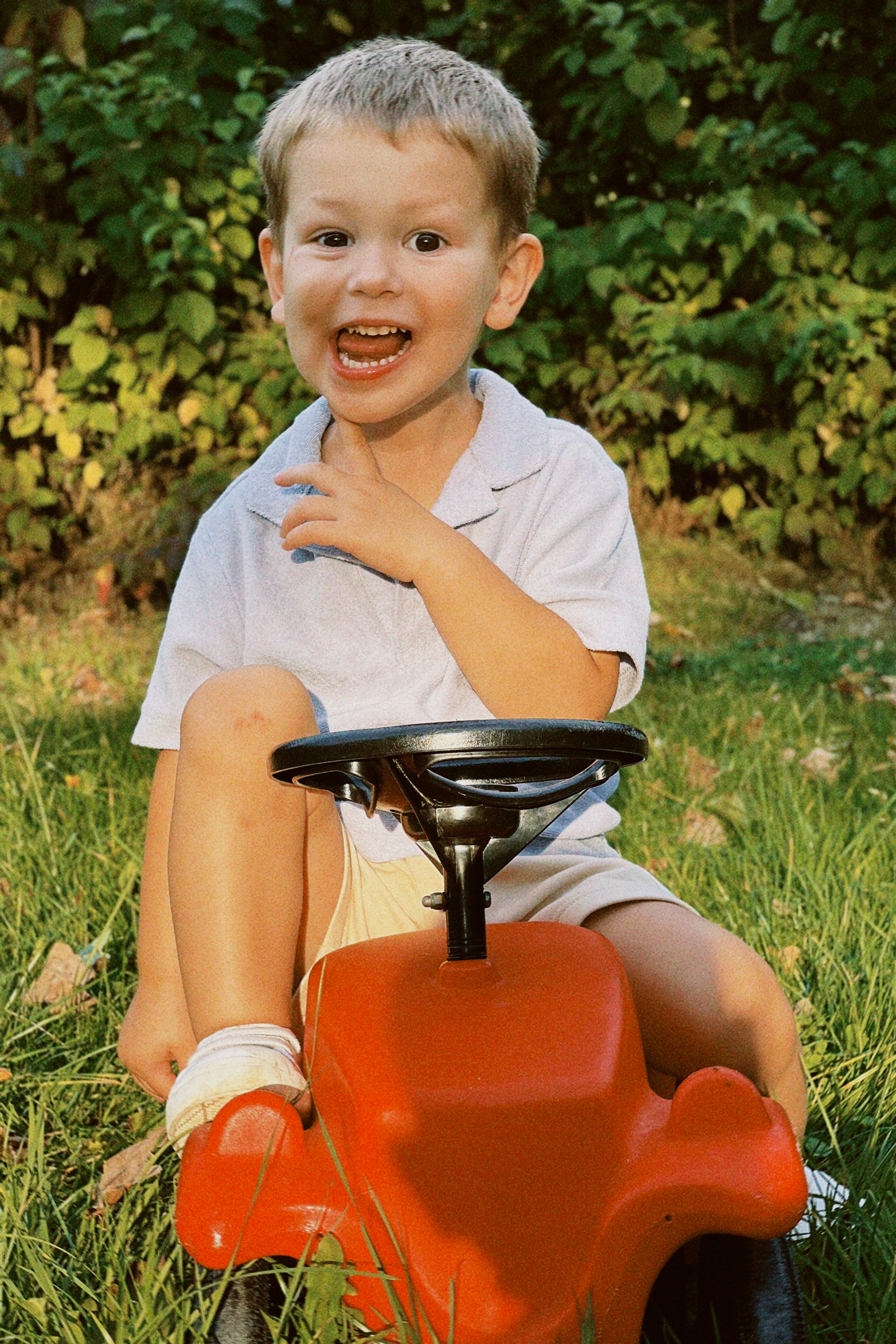 Joyful child enjoying a ride on a red toy car in a garden setting.