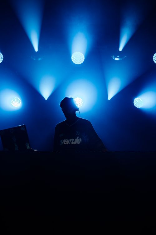 Free Silhouette of a DJ performing under vibrant blue stage lights, creating an energetic atmosphere. Stock Photo