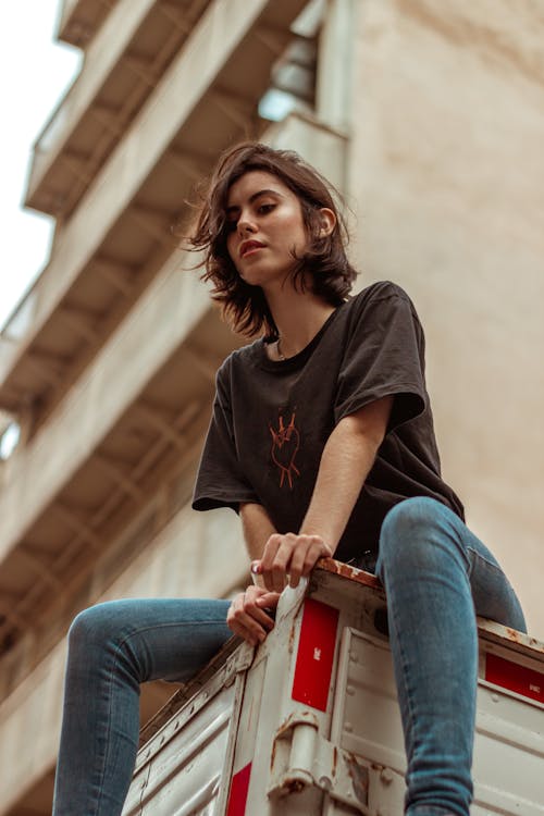 Woman in Black Crew Neck T-shirt and Blue Denim Jeans Sitting on Brown Wooden Bench