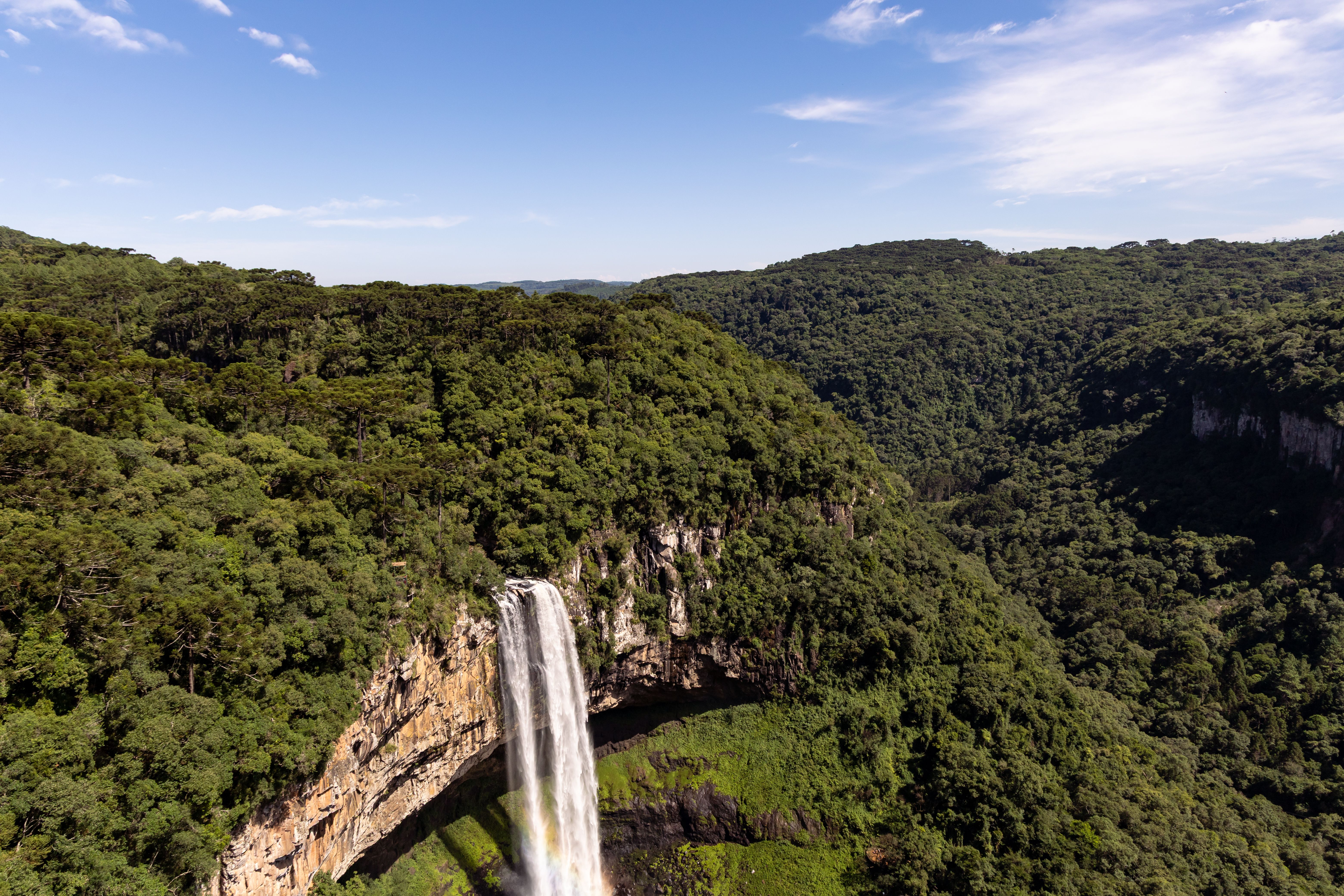 Stunning aerial view of Caracol Falls in Gramado, Brazil with lush green forest and clear sky.
