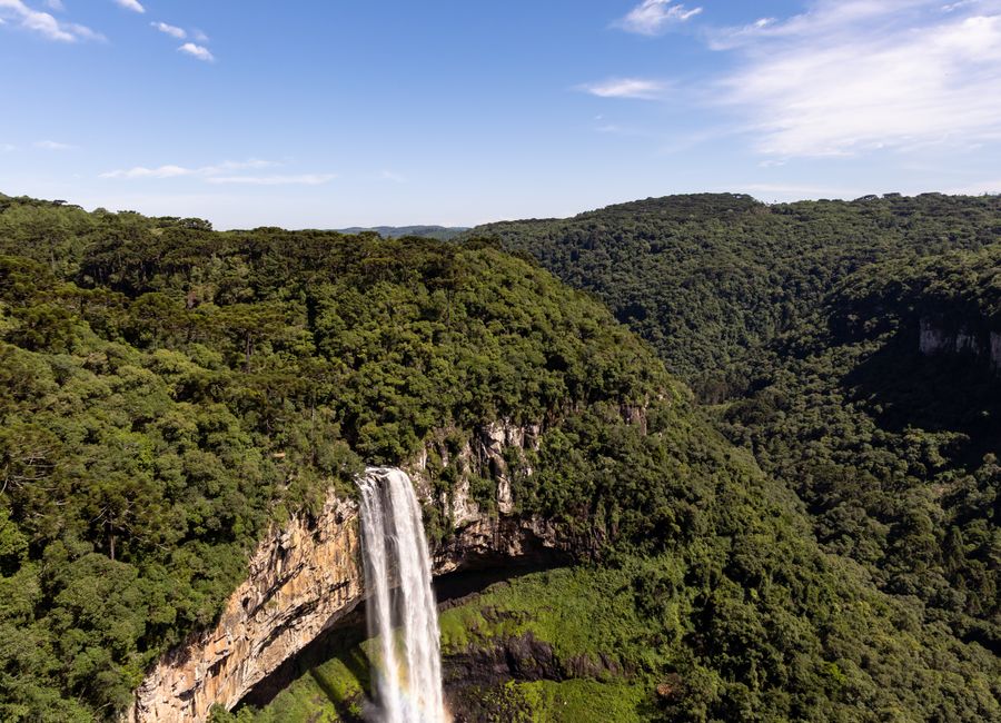 Stunning aerial view of Caracol Falls in Gramado, Brazil with lush green forest and clear sky.