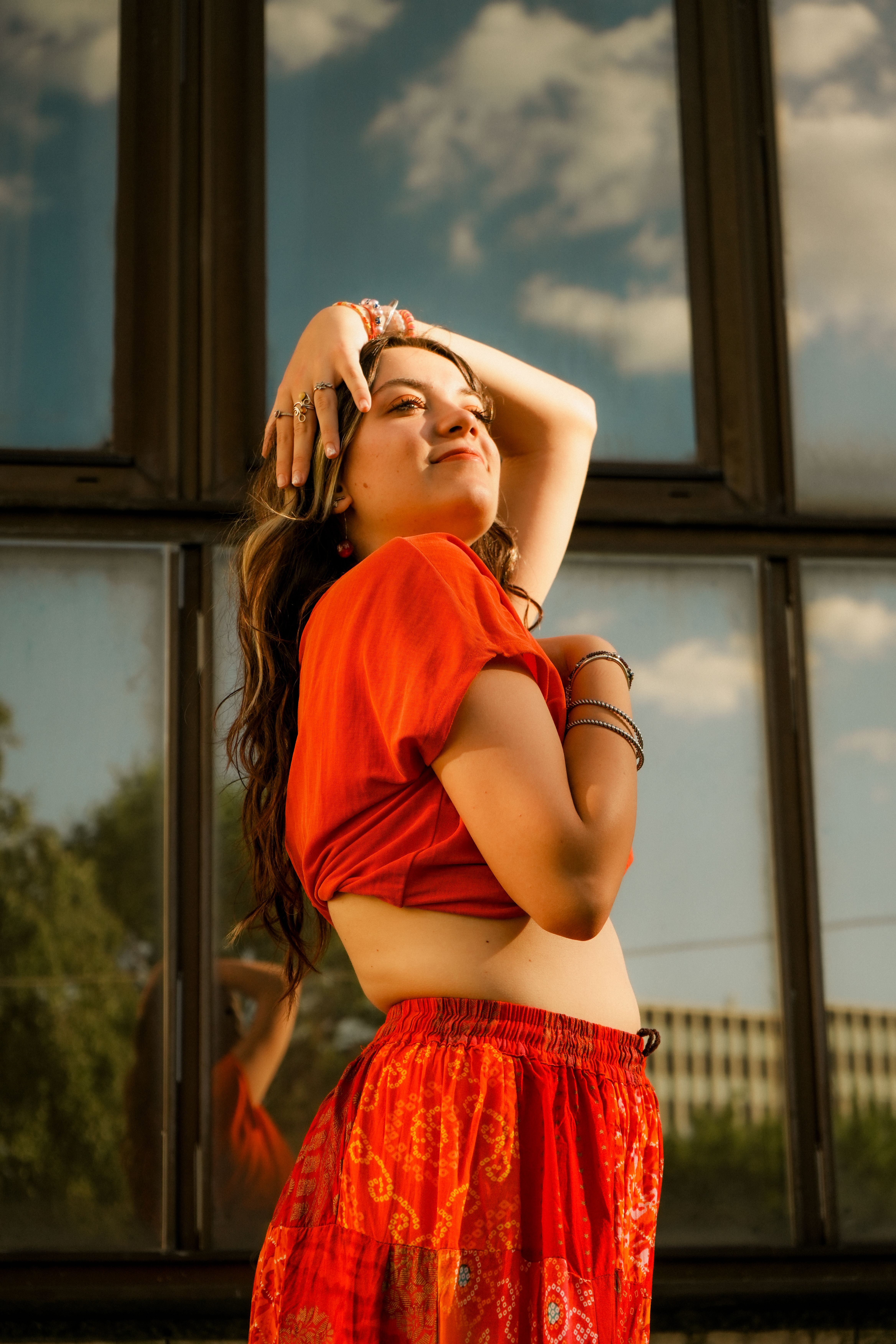 Confident young woman posing outdoors in bright red attire against a reflective window.