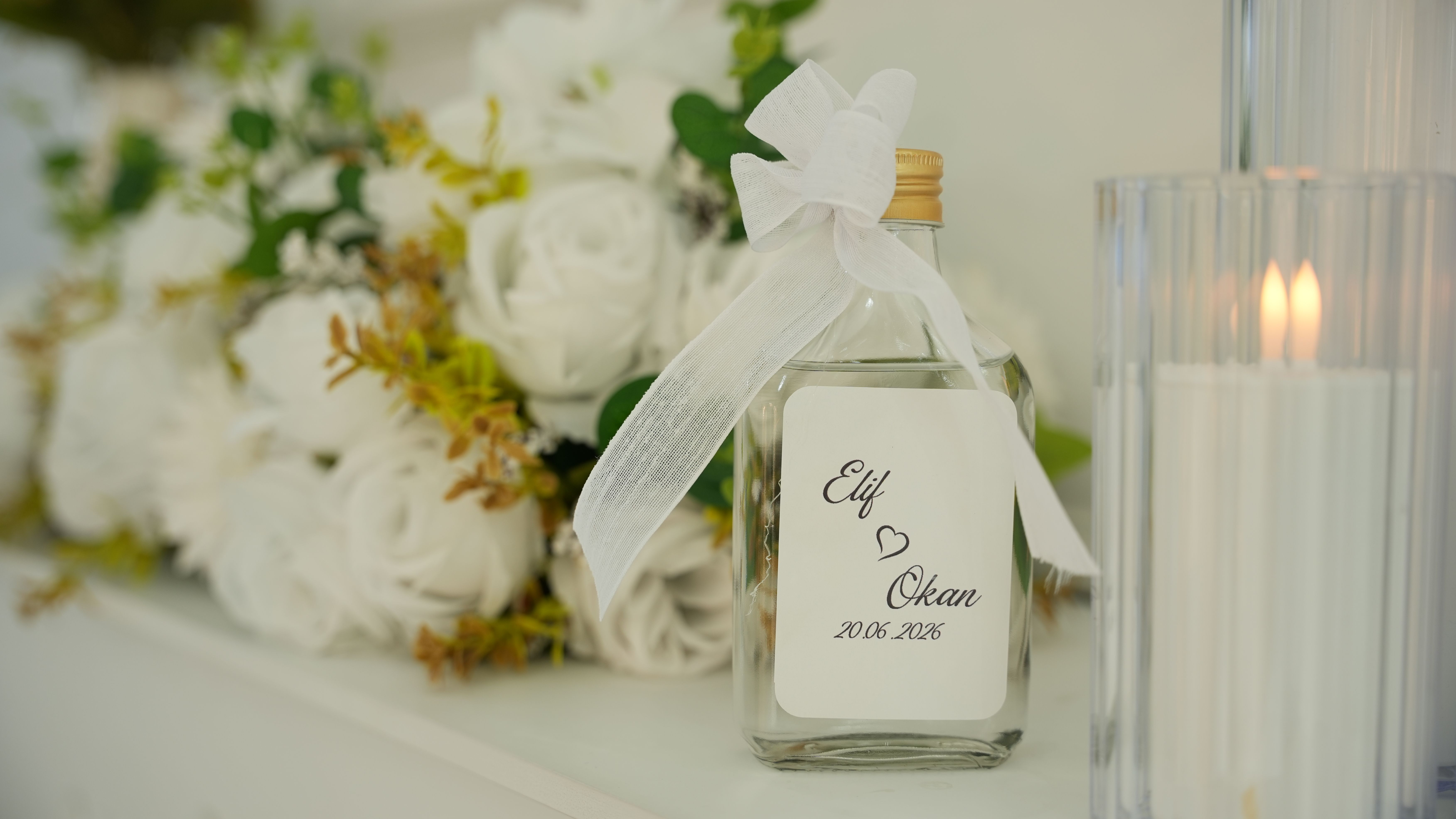 Luxurious wedding setting with white roses, candles, and personalized glass bottle.