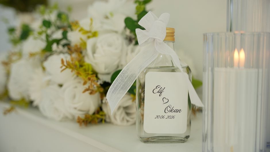Luxurious wedding setting with white roses, candles, and personalized glass bottle.