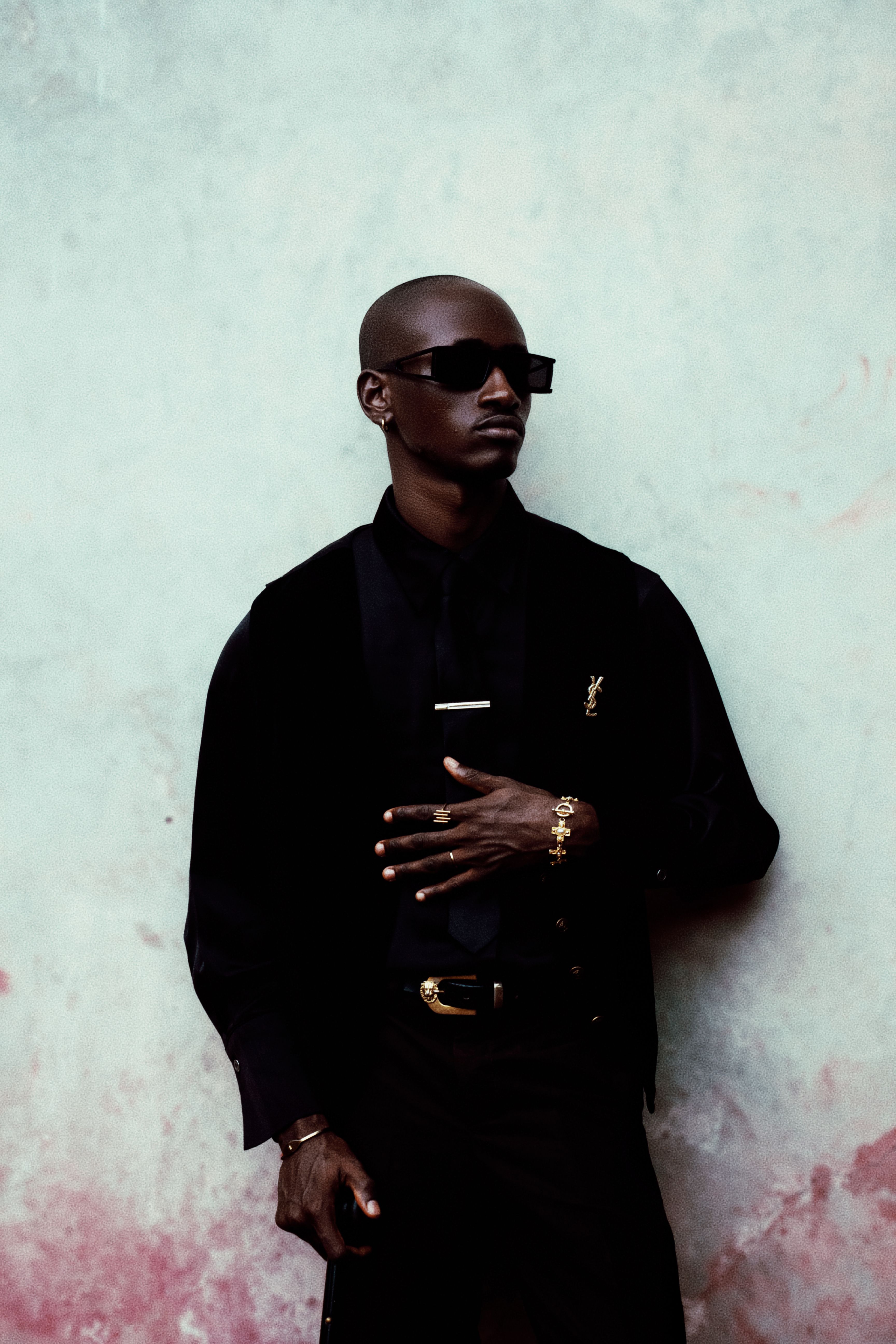 Elegant man in black wearing sunglasses and gold accessories. Fashionable and modern look.