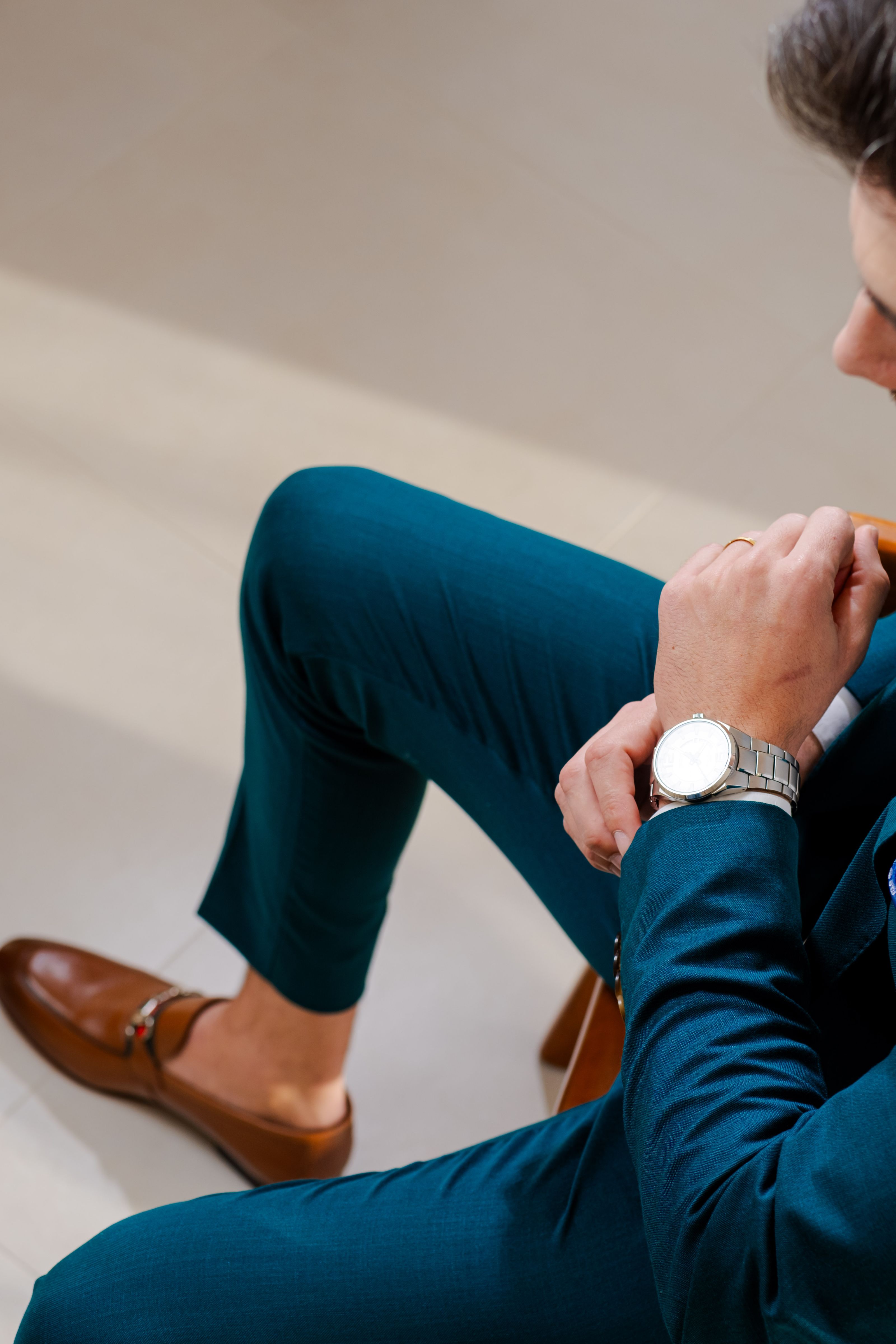 Homem vestindo um traje verde-água, mocassins marrons e um relógio de luxo em um ambiente moderno.