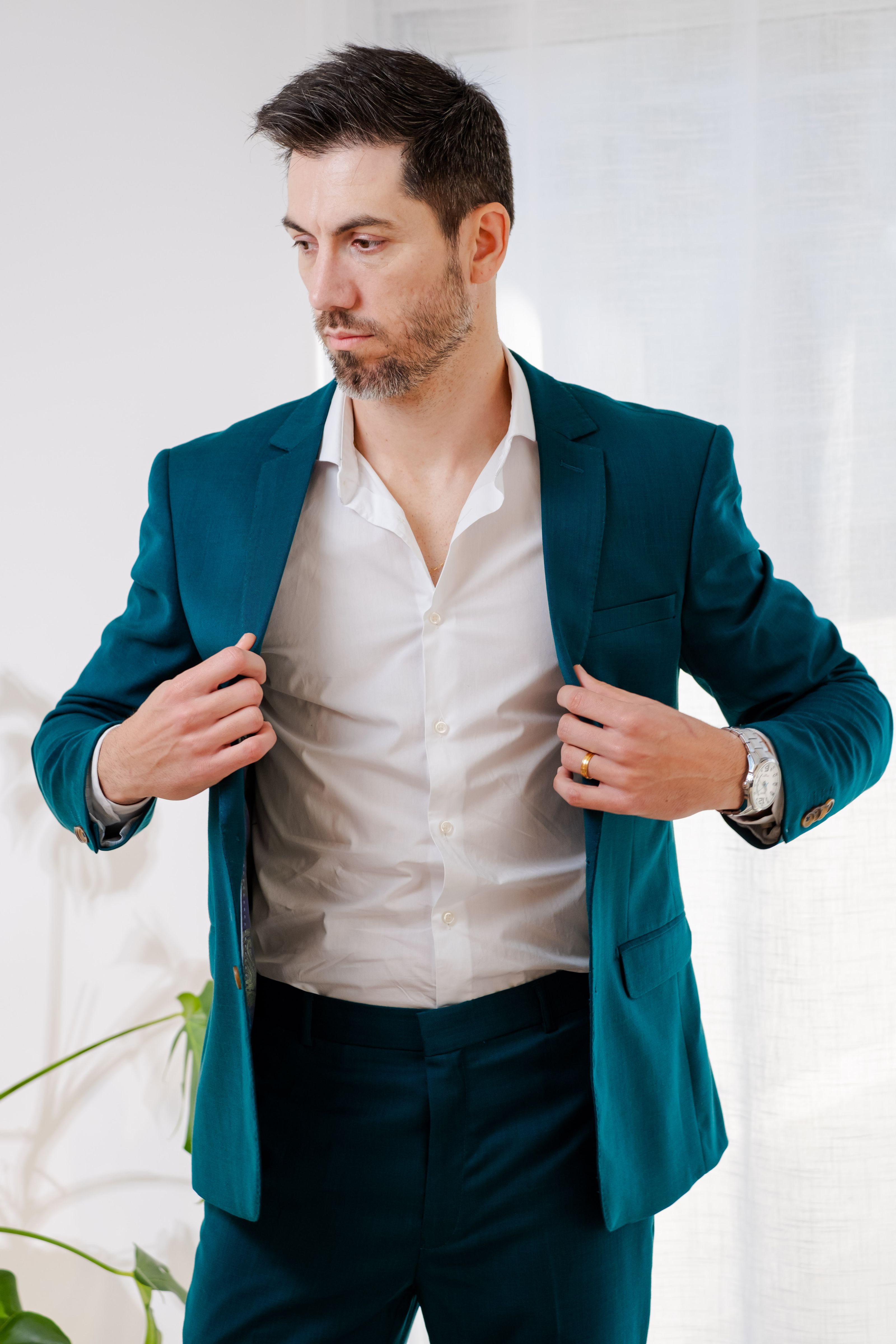 Um homem moderno, vestindo um terno azul-petróleo, ajusta o paletó em um ambiente interno bem iluminado, exalando confiança e estilo.