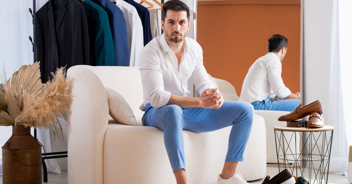 A fashionable man in a modern showroom with elegant outfits and shoes displayed around him.