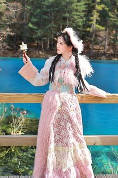 Woman in traditional clothing overlooking a vibrant turquoise lake outdoors.