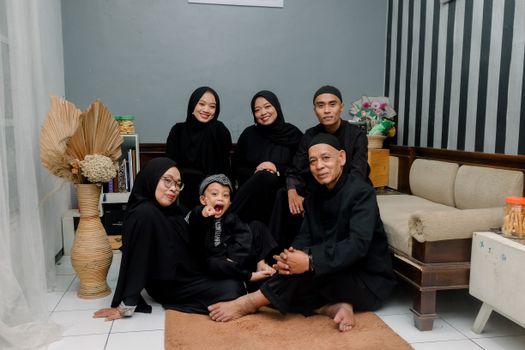 A family of six in traditional black attire posing in a living room setting. - Fotografer Sidoarjo