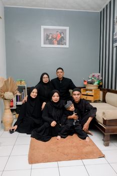 A family of six dressed in black gathered for a group portrait in a cozy room. - Fotografer Sidoarjo