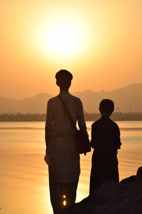 Free Serene sunset silhouette of two people by a lake in Islamabad, Pakistan. Stock Photo
