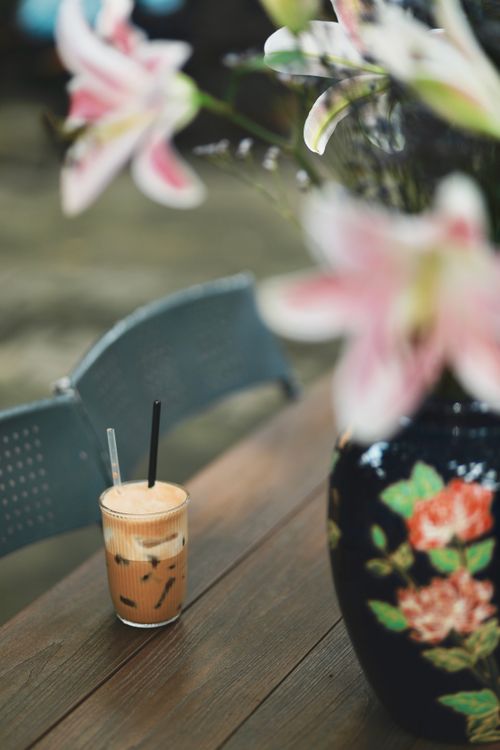 Free Chilled iced coffee on wooden table next to floral vase on an outdoor patio. Stock Photo