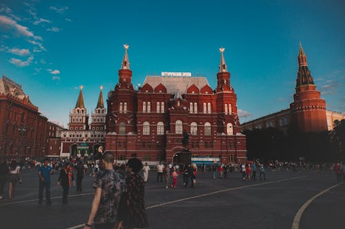 Exterior of square with tourists walking near State Historical Museum building in Red Square Moscow Russia under blue cloudy sky