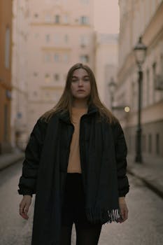 黄昏时分，一名穿着温暖衣服的年轻女子站在城市街道上，表情沉思