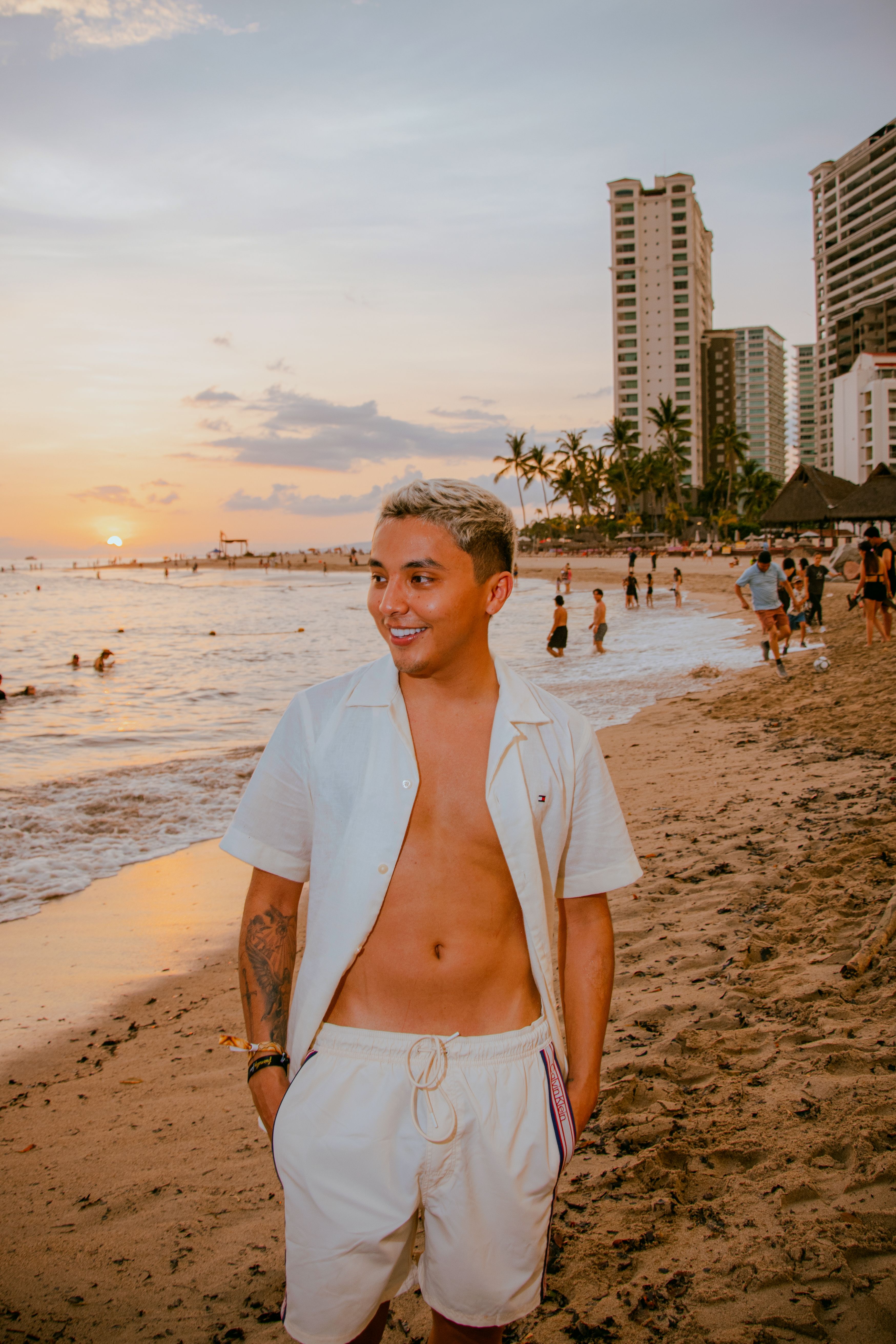 A young man enjoys a vibrant sunset on the beach in Puerto Vallarta, Mexico, with scenic coastal views and modern skyline.