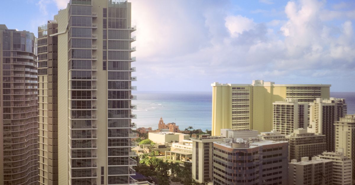 Photo by Alec Doualetas Downtown Honolulu skyline with high-rise buildings and ocean view under a blue sky.