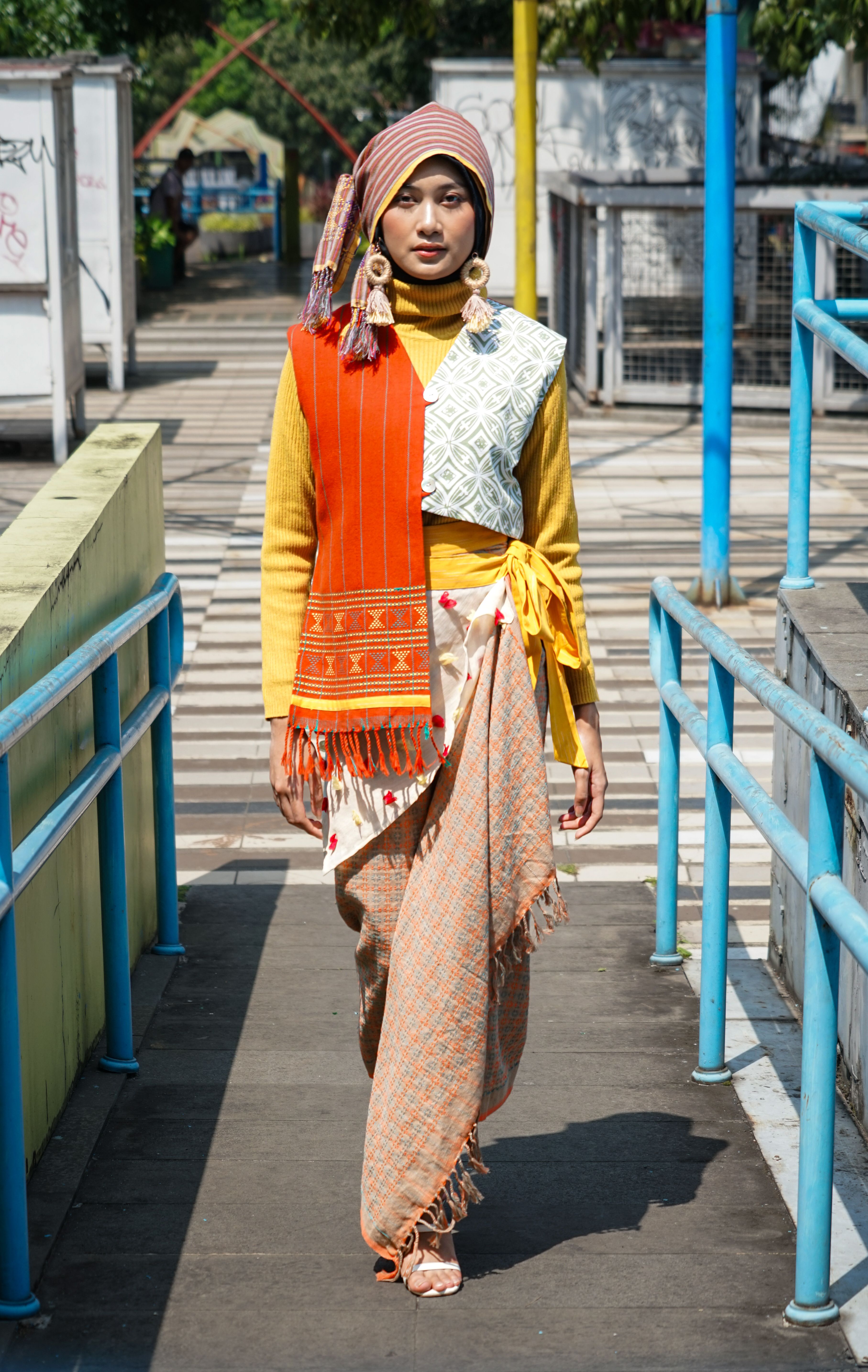 A woman in vibrant traditional and modern attire on a street in Bandung, Indonesia.