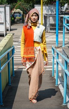 A woman in vibrant traditional and modern attire on a street in Bandung, Indonesia.