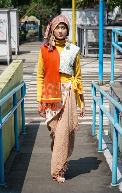 A woman in vibrant traditional and modern attire on a street in Bandung, Indonesia.