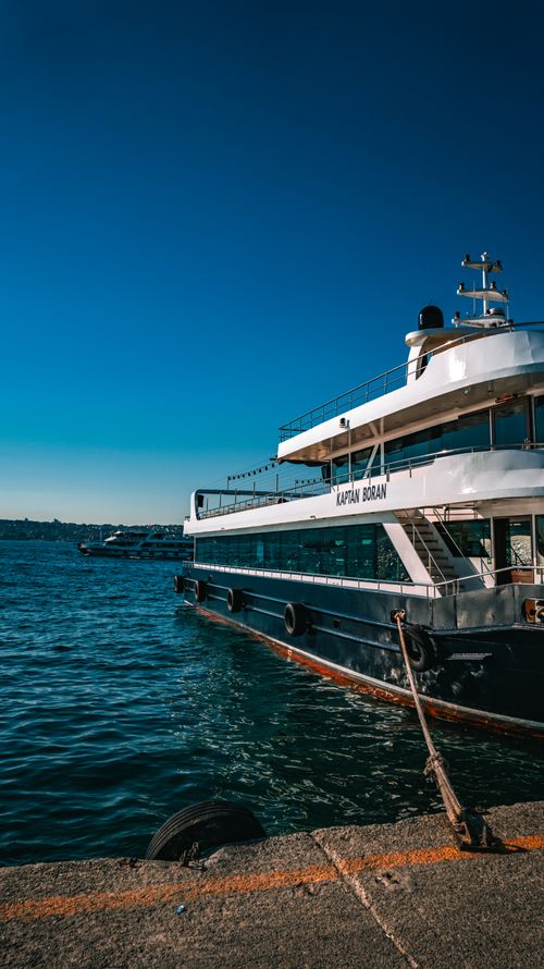 Free A passenger ferry named 'Kaptan Boran' docked at a scenic waterfront under a clear blue sky. Stock Photo