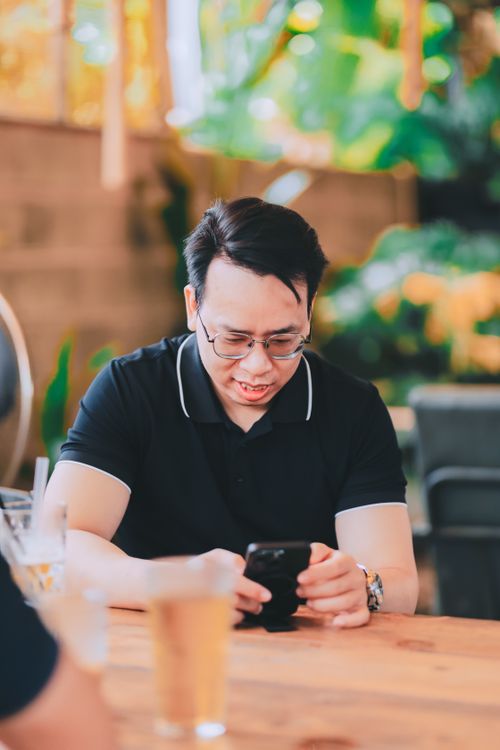 Free An adult male using a smartphone at an outdoor café, with drinks on the table. Stock Photo