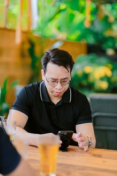Man focused on smartphone at a cozy outdoor garden café table. - Fotografer Sidoarjo