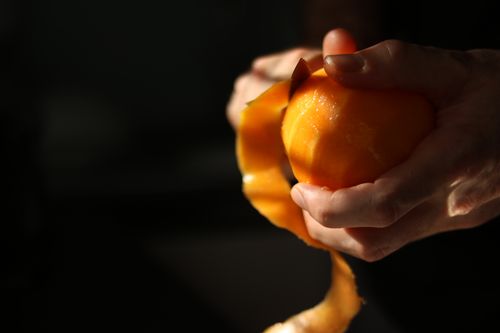 Free Hands peeling a vibrant orange in natural light creating a warm, artistic composition. Stock Photo