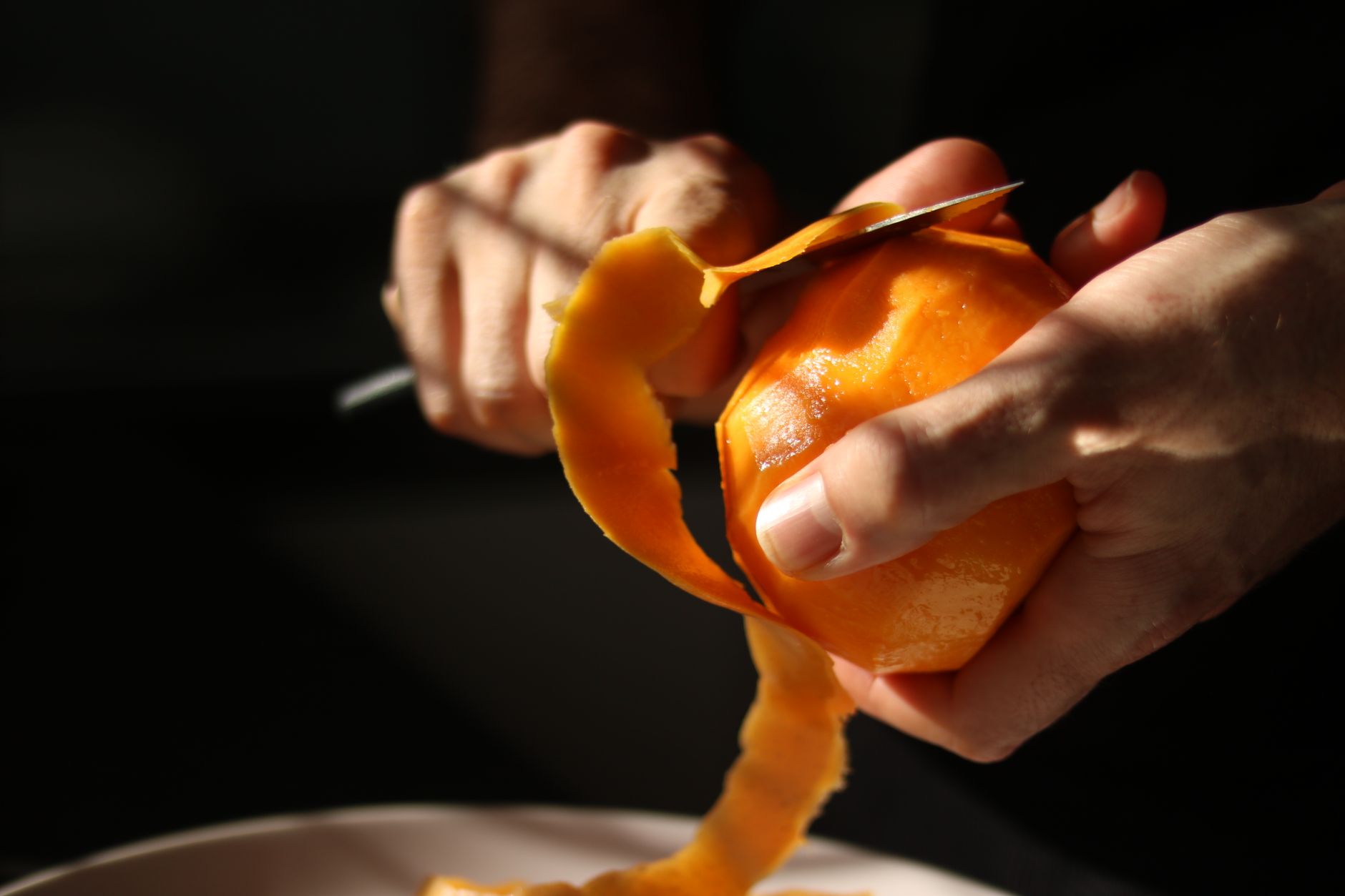 Detailed view of hands skillfully peeling a bright orange fruit, casting natural shadows.
