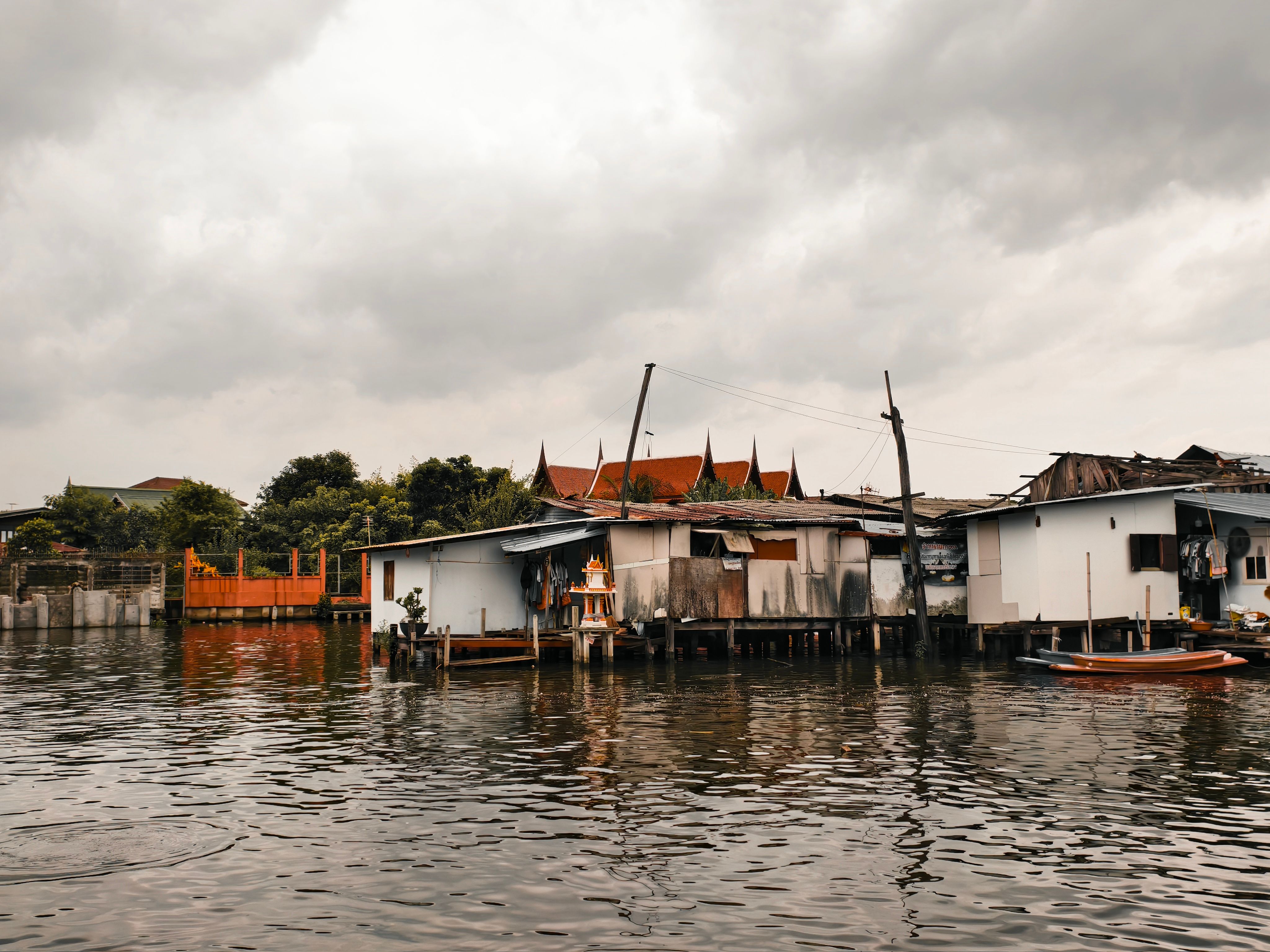 Traditional stilt houses by a canal in Bangkok under overcast skies, showcasing local architecture.