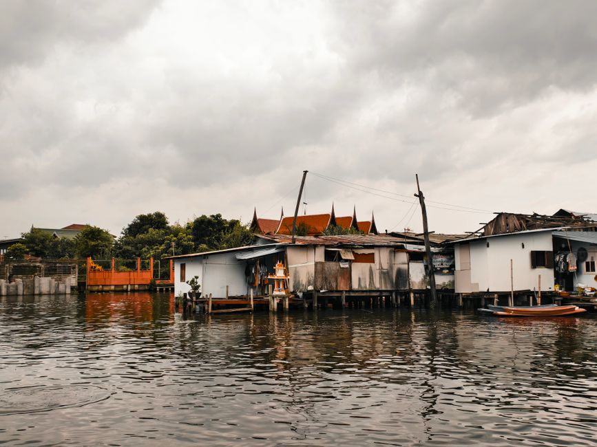 Traditional stilt houses by a canal in Bangkok under overcast skies, showcasing local architecture.