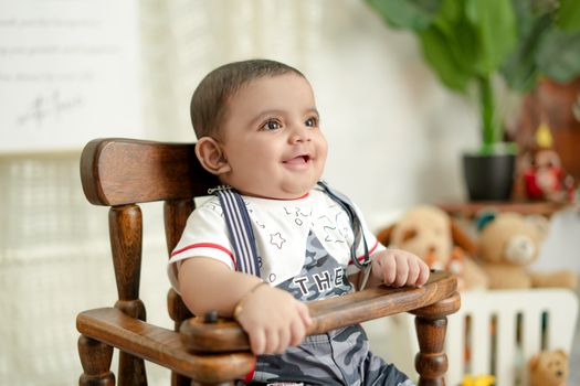 Smiling baby sits in a wooden high chair surrounded by toys in a bright indoor setting.