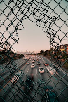 日落时分，车流在一条由破碎栅栏围成的高速公路上涌动，展现出旧金山的城市景观