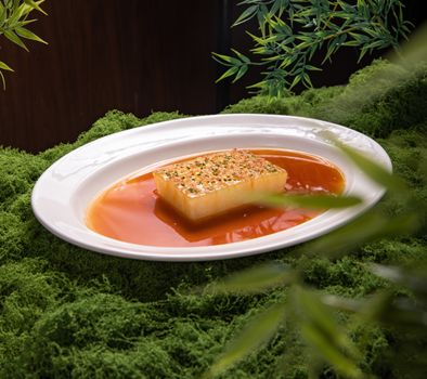 Gourmet tofu cube on a bed of moss, drizzled with savory sauce, elegant plating.