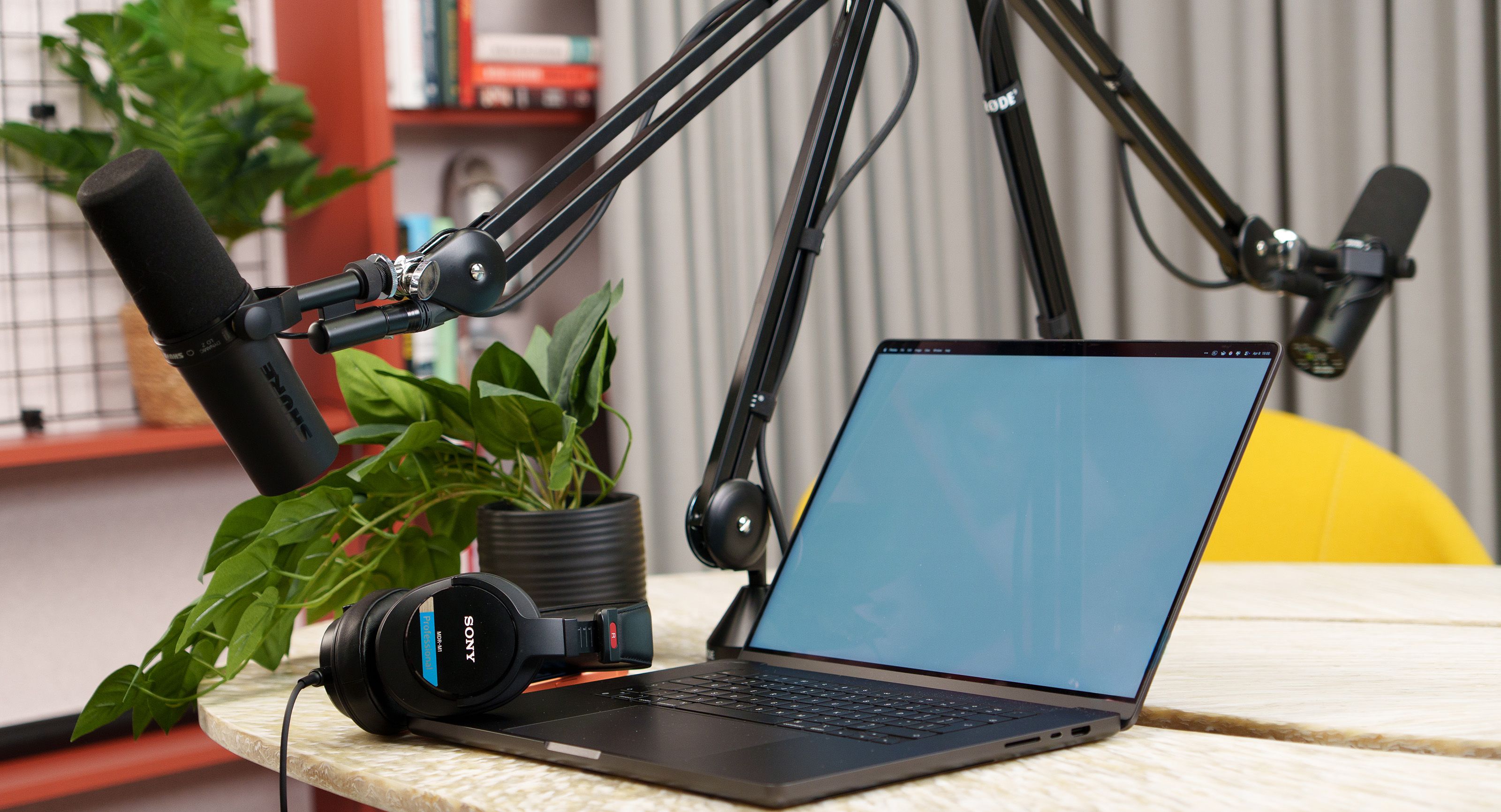 A modern podcast recording studio with a laptop, microphones, and headphones on a desk.