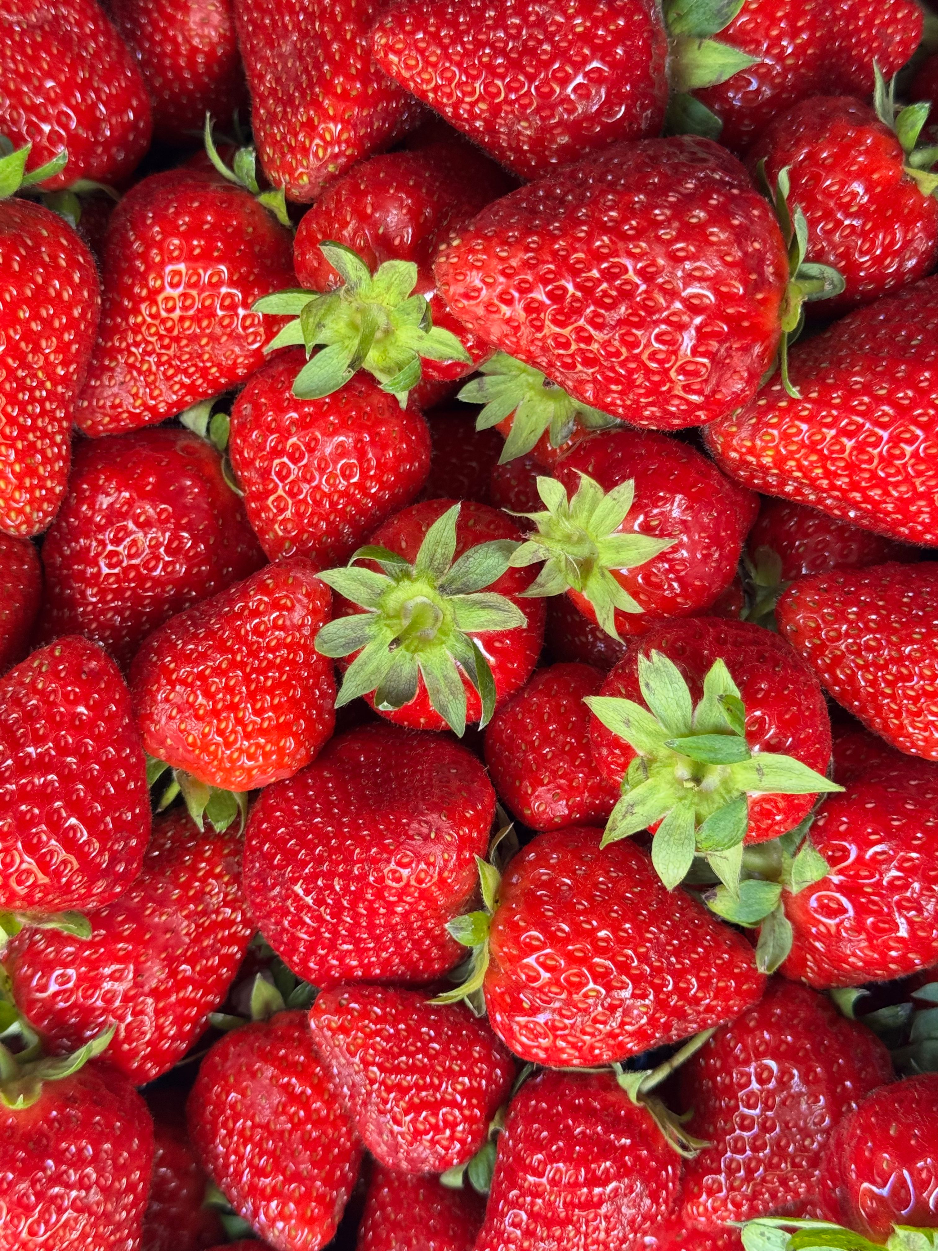 A vibrant close-up image of fresh, ripe red strawberries with green leaves.