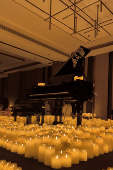 Dimly lit room with a grand piano and numerous glowing candles creating a serene ambiance.