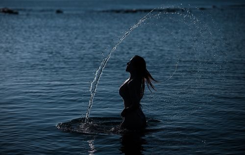 Free Silhouette of a woman flipping hair in the water at sunset, creating a water arc. Stock Photo