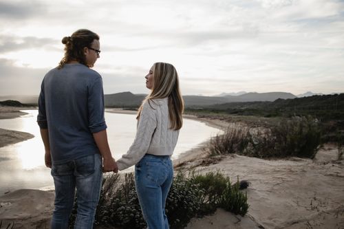Free Romantic couple holding hands at sunset by a tranquil river, surrounded by nature. Stock Photo