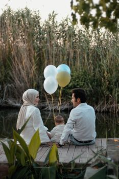 A family enjoys a tranquil moment by the lake with balloons, surrounded by nature.