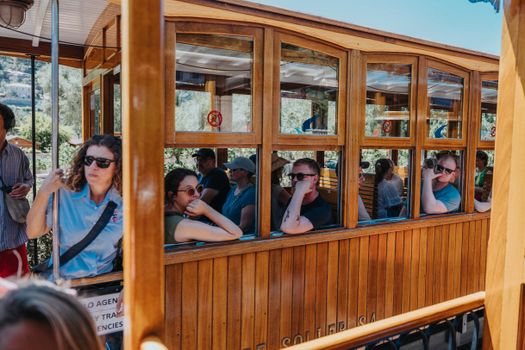 A group of tourists rides a traditional wooden tram in a scenic outdoor setting, enjoying the summer view.