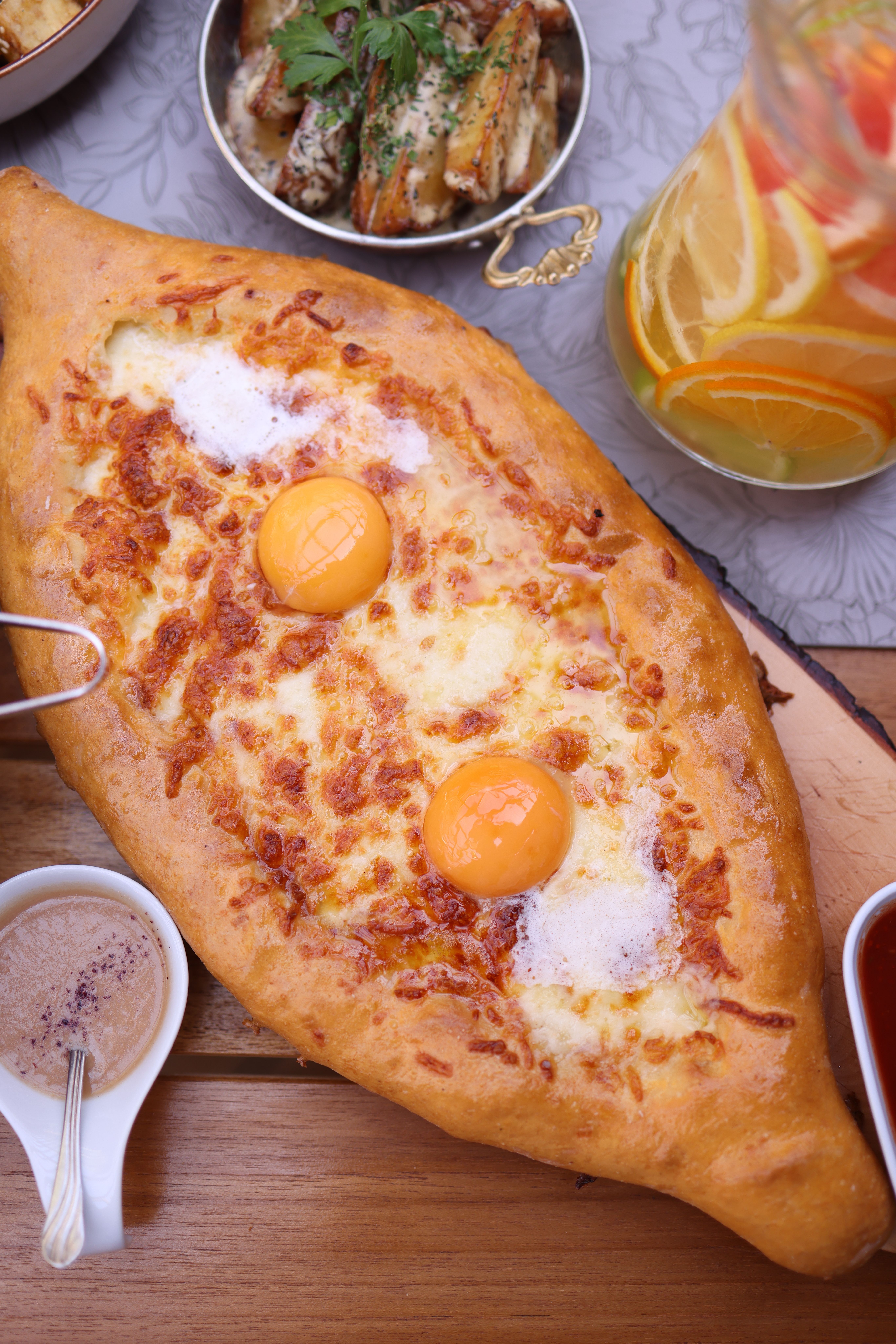 Top view of traditional Georgian khachapuri filled with cheese and eggs, surrounded by appetizers and drinks.