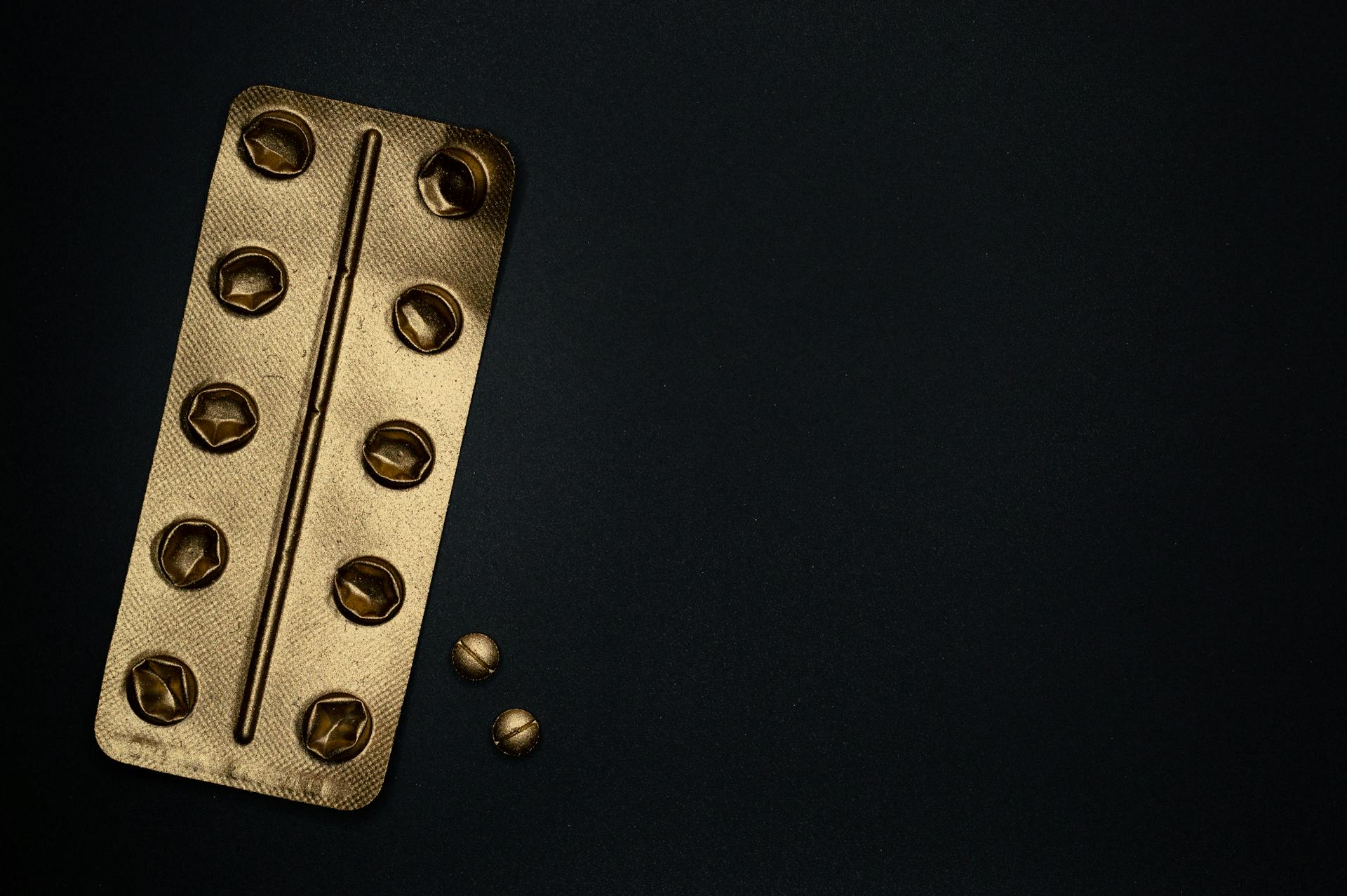 Gold Blister Pack and Tablets on Black Surface