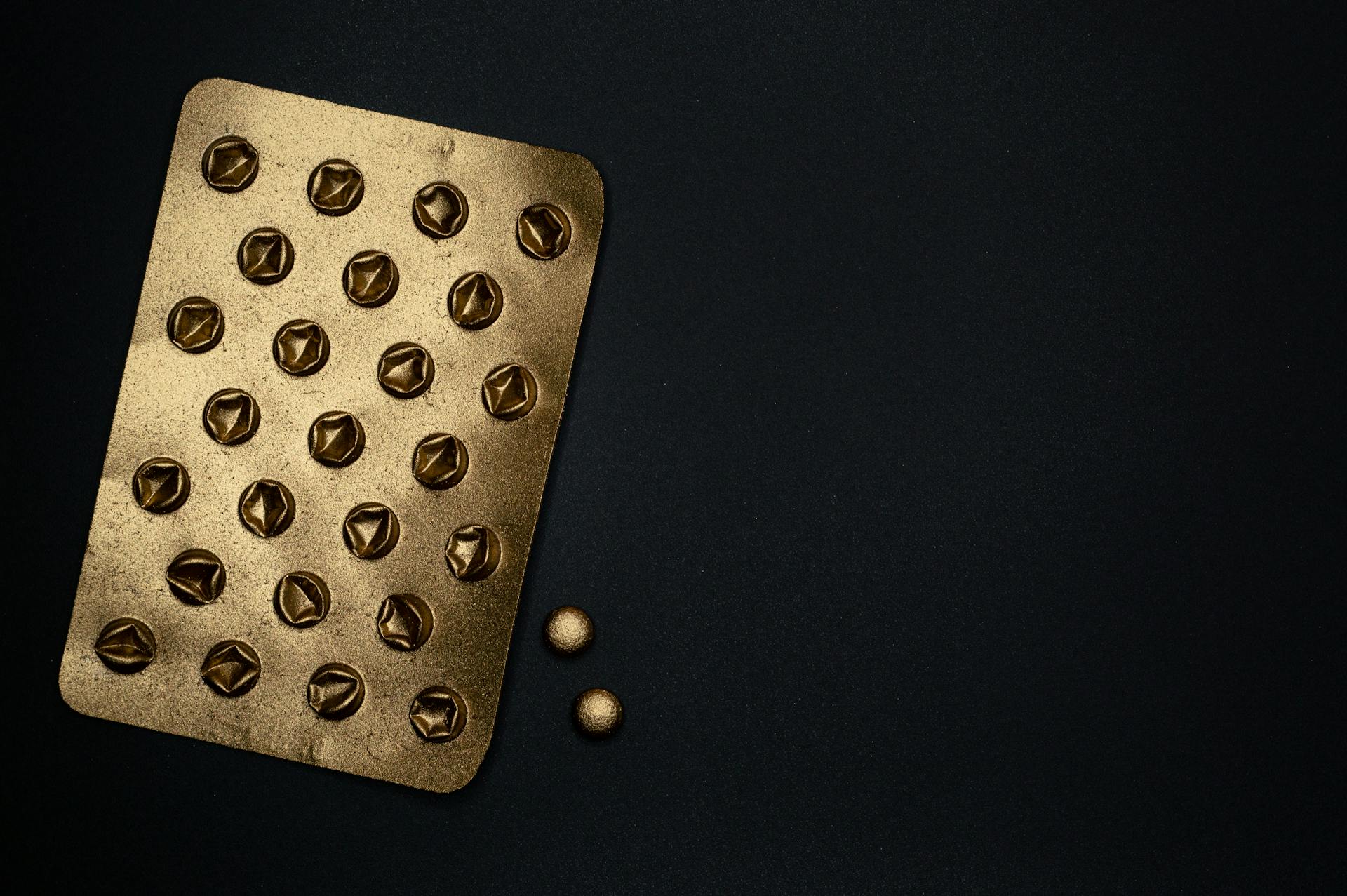 A close-up of a gold metallic blister pack on a black surface, ideal for healthcare themes.