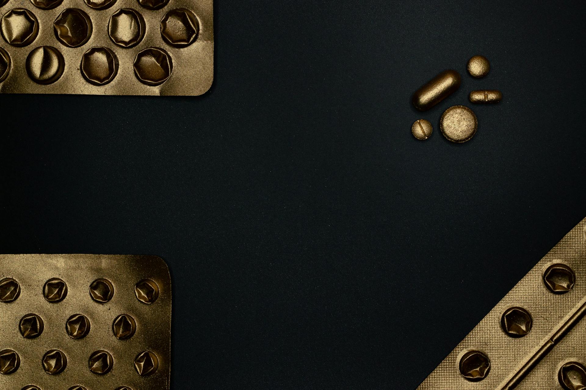 Golden blister packs and pills on a dark surface, offering contrast and copyspace.