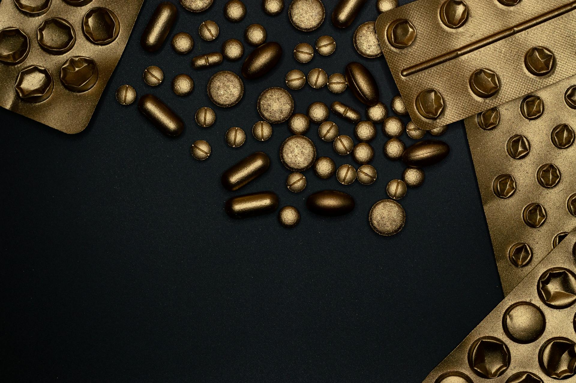 Close-up of gold blister packs and pills arranged on a black surface.