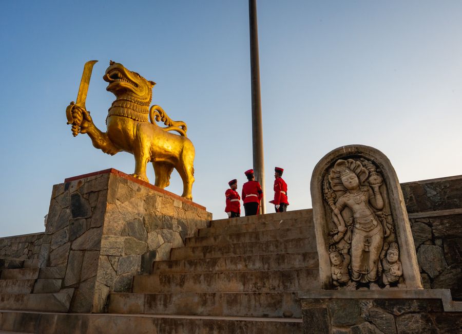 Three uniformed guards stand near the golden lion statue in Colombo at sunset.